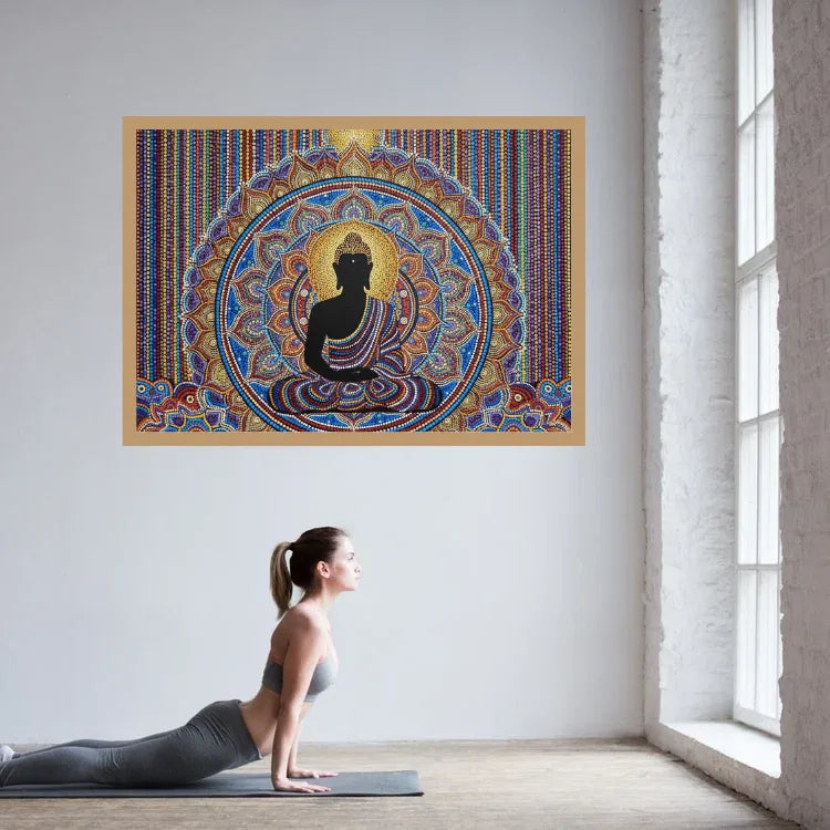 A colorful framed wall art print featuring a seated Buddha silhouette with intricate mandala-style patterns, displayed on a white wall in a bright room. A woman in athletic wear is lying on a yoga mat below, in a yoga pose.