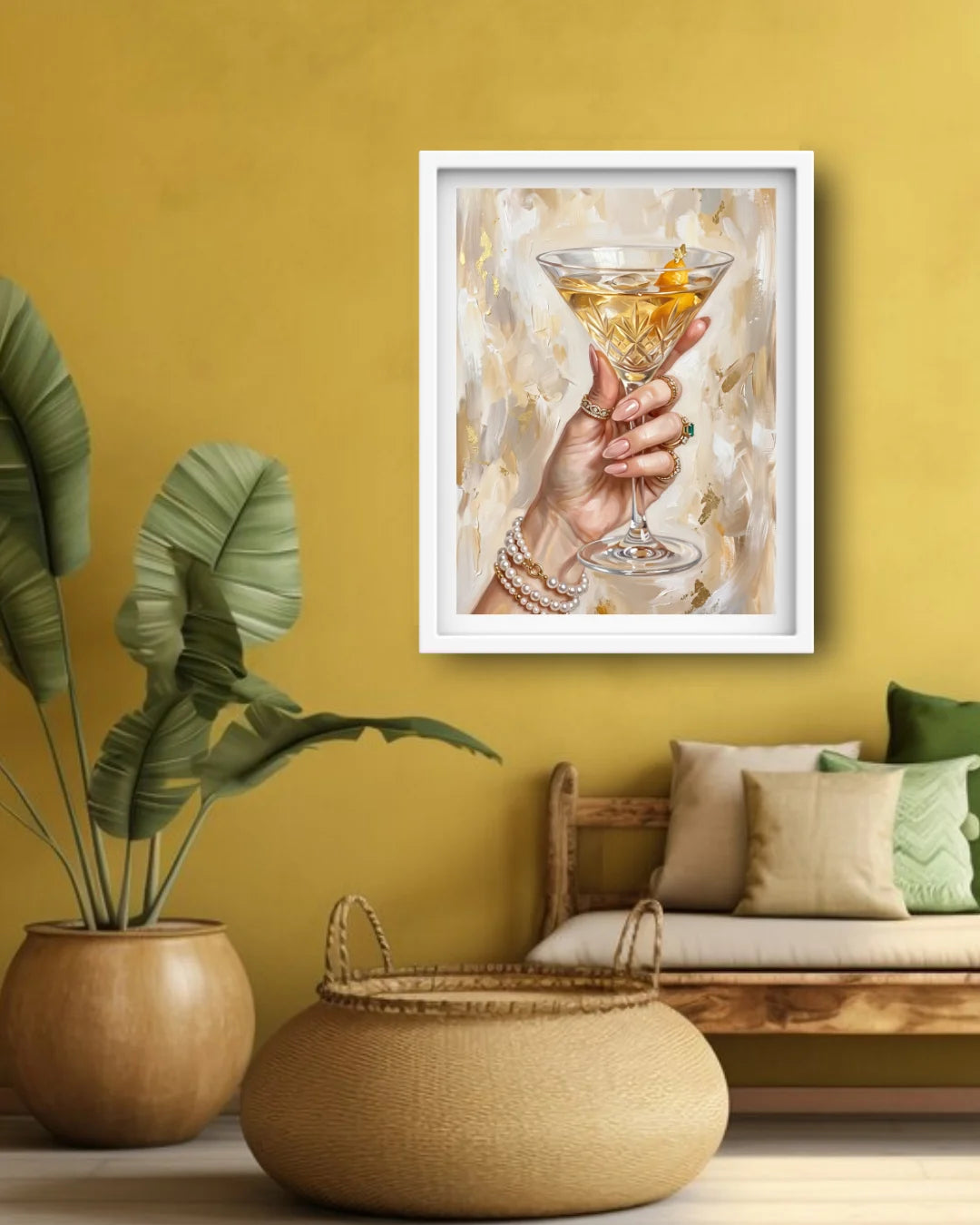 A framed art print depicting a hand holding a martini glass with a gold citrus twist, displayed on a mustard yellow wall in a styled living room setting with a bench, pillows, and a potted plant.
