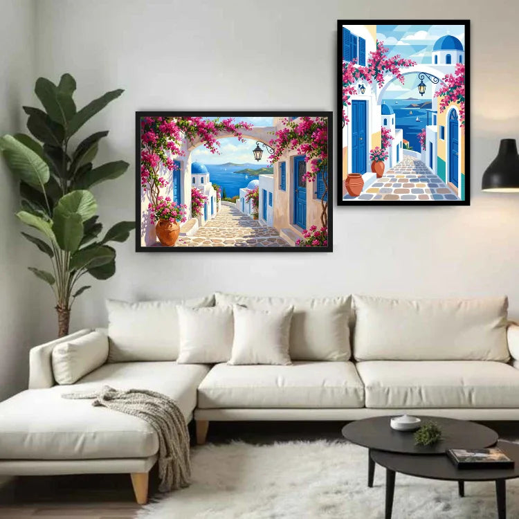 Two framed paintings of a blue and white Mediterranean village street with pink bougainvillea flowers hang on a white wall above a beige sectional sofa in a modern living room.