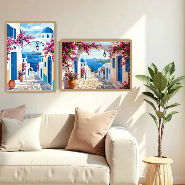Two framed paintings of a Mediterranean street scene with blue domes, white buildings, and pink bougainvillea flowers, displayed on a wall above a beige sofa in a styled living room.