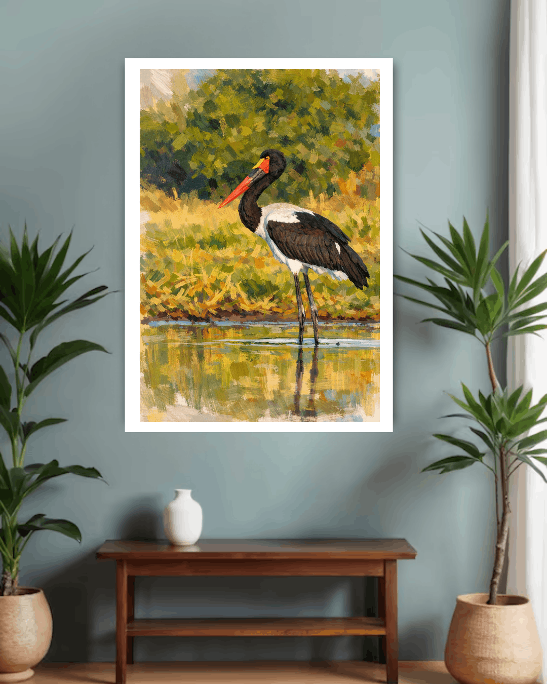 Framed painting of a bird by a lake on a wall with plants and a table below.