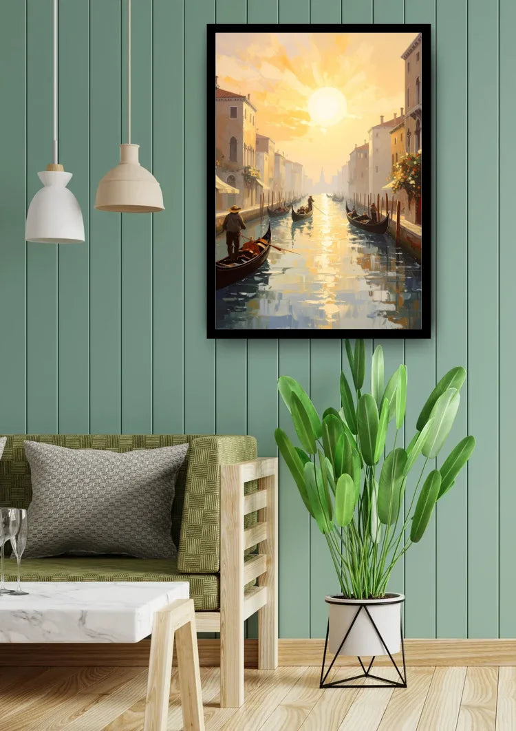 A framed vertical canvas painting of a Venice canal at sunset hangs on a green paneled wall above a wooden bench with a green cushion, next to a potted plant.