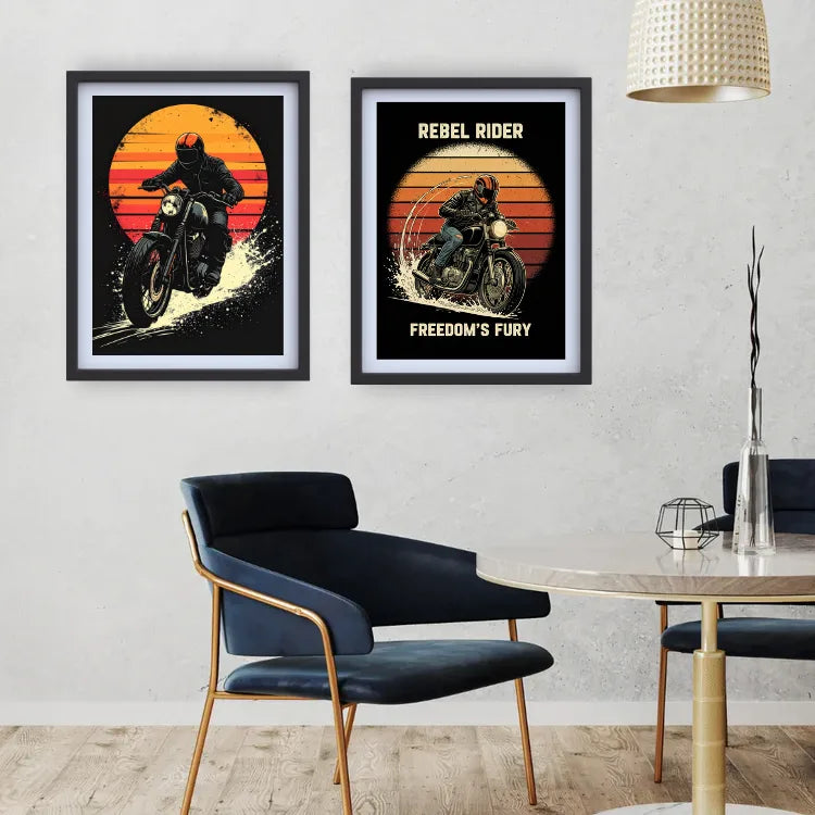 Two framed biker art prints hang on a light gray wall above a dark blue chair and a round table in a modern room. The prints feature retro sunset designs with a motorcycle rider, one with the text &