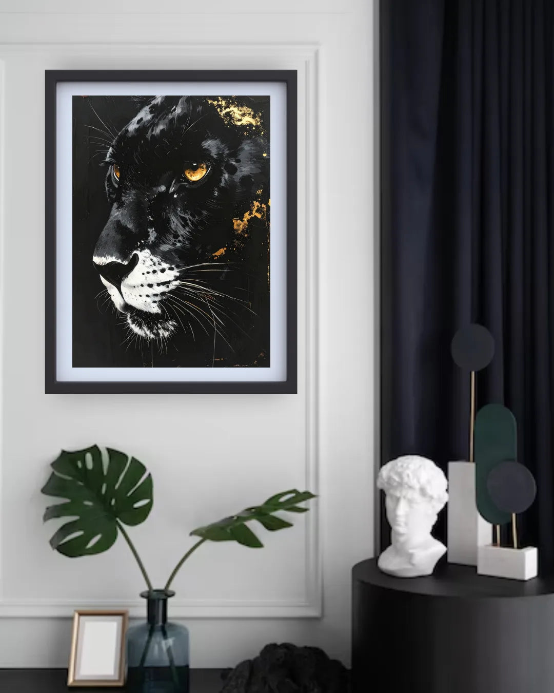 A framed black panther art print with gold leaf accents hangs on a white wall in a styled room setting with a dark curtain, a blue vase with a monstera leaf, and a white bust on a side table.