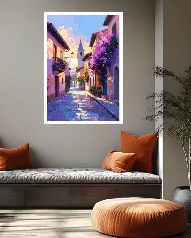 A vertical framed art print depicting a colorful, impressionistic European street scene with purple flowers and a church tower, displayed on a gray wall above a modern daybed in a styled living room.