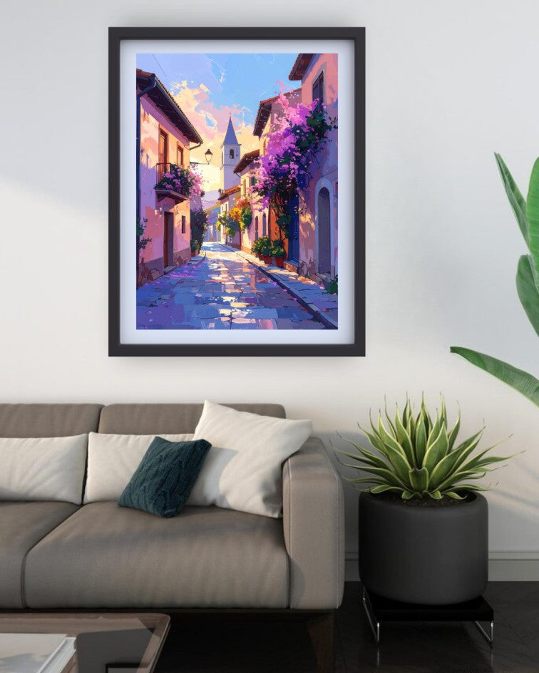 A framed art print depicting a colorful, impressionistic European village street with purple flowers and a church spire, displayed on a white wall above a modern gray sofa in a living room setting.