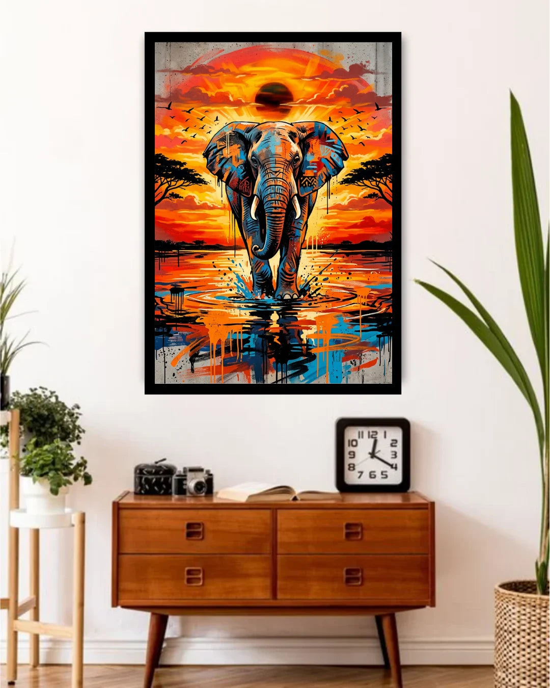 Framed artwork of an elephant at sunset over water, displayed on a wall above a wooden console table.