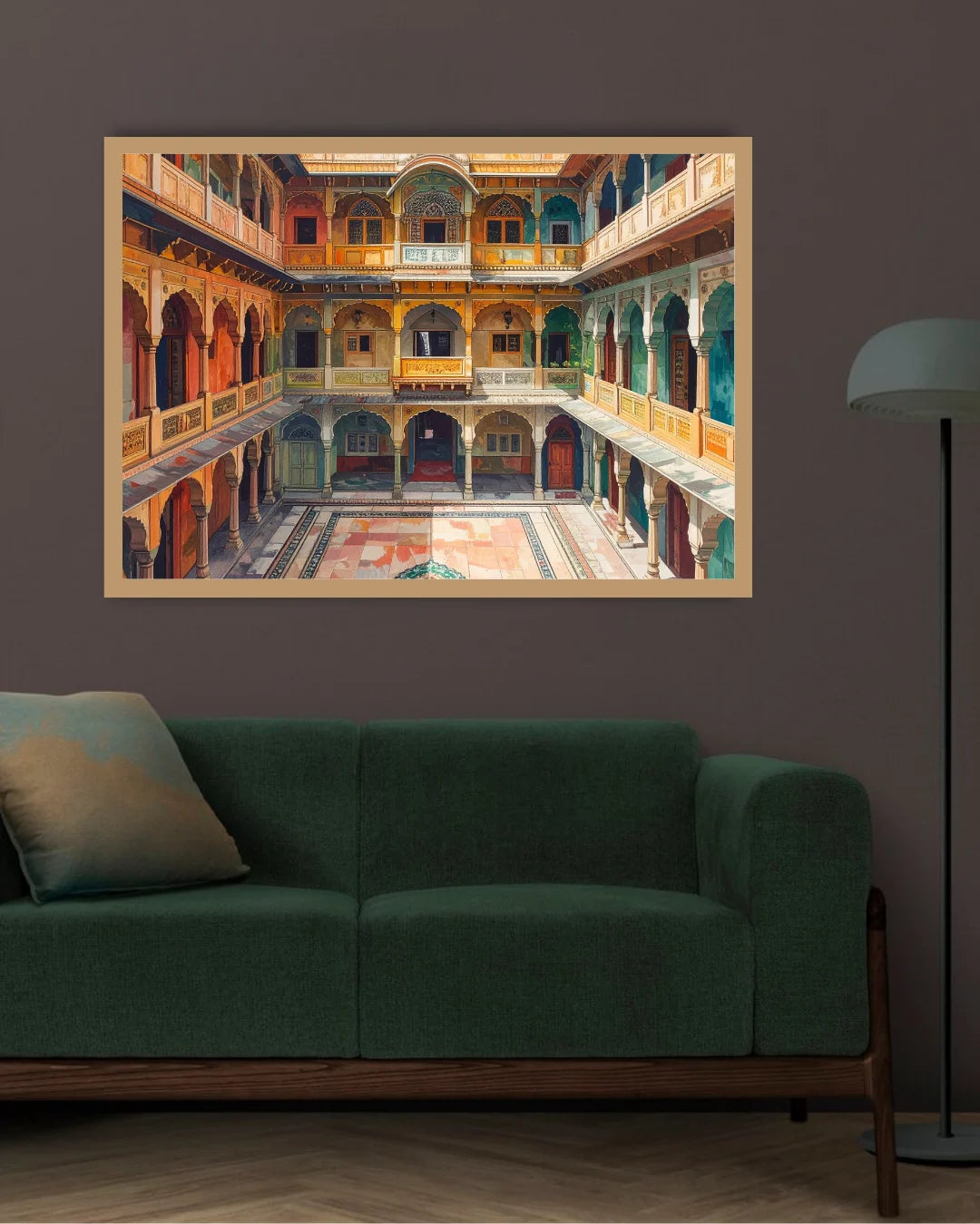 A framed art print depicting a colorful courtyard with arches and balconies, displayed on a dark wall above a green sofa in a modern living room setting.