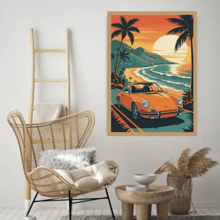 A framed art print featuring a retro orange sports car on a tropical beach sunset road trip, styled in a modern living room setting next to a wicker chair and wooden ladder.