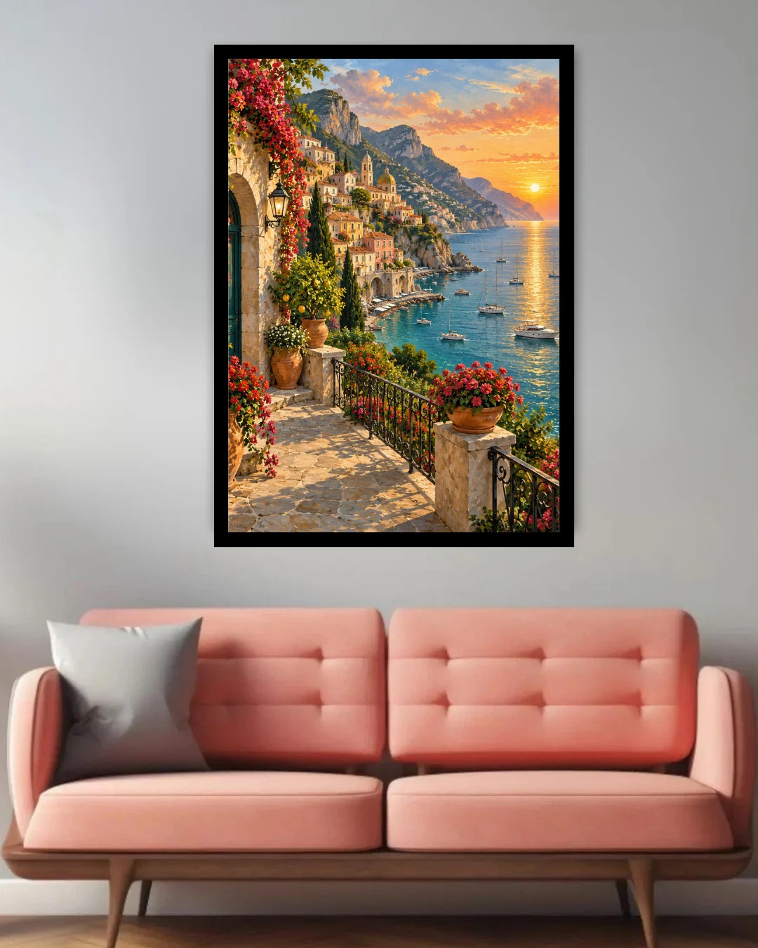 A framed vertical canvas print of a Mediterranean coastal town at sunset, hung on a light gray wall above a pink tufted sofa.