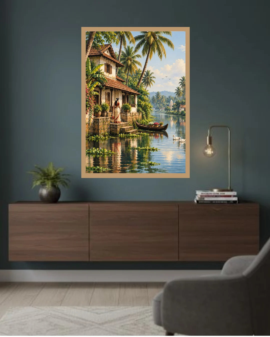 A framed landscape art print depicting a tropical lakeside village with palm trees, a house, and a boat, displayed on a dark blue-gray wall above a wooden console table in a styled room.
