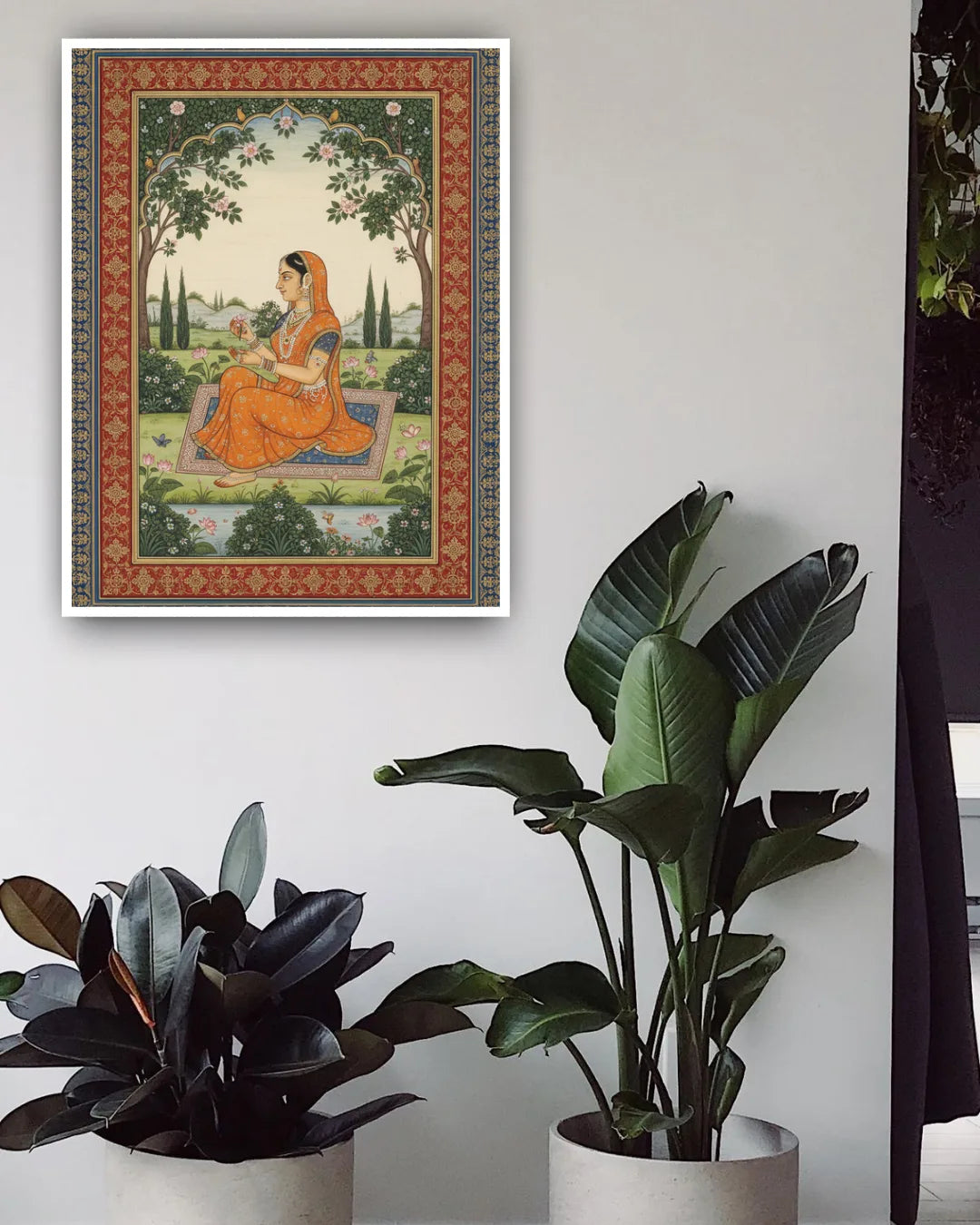 Framed traditional artwork of a woman in an orange dress sitting on a rug, with potted plants below.