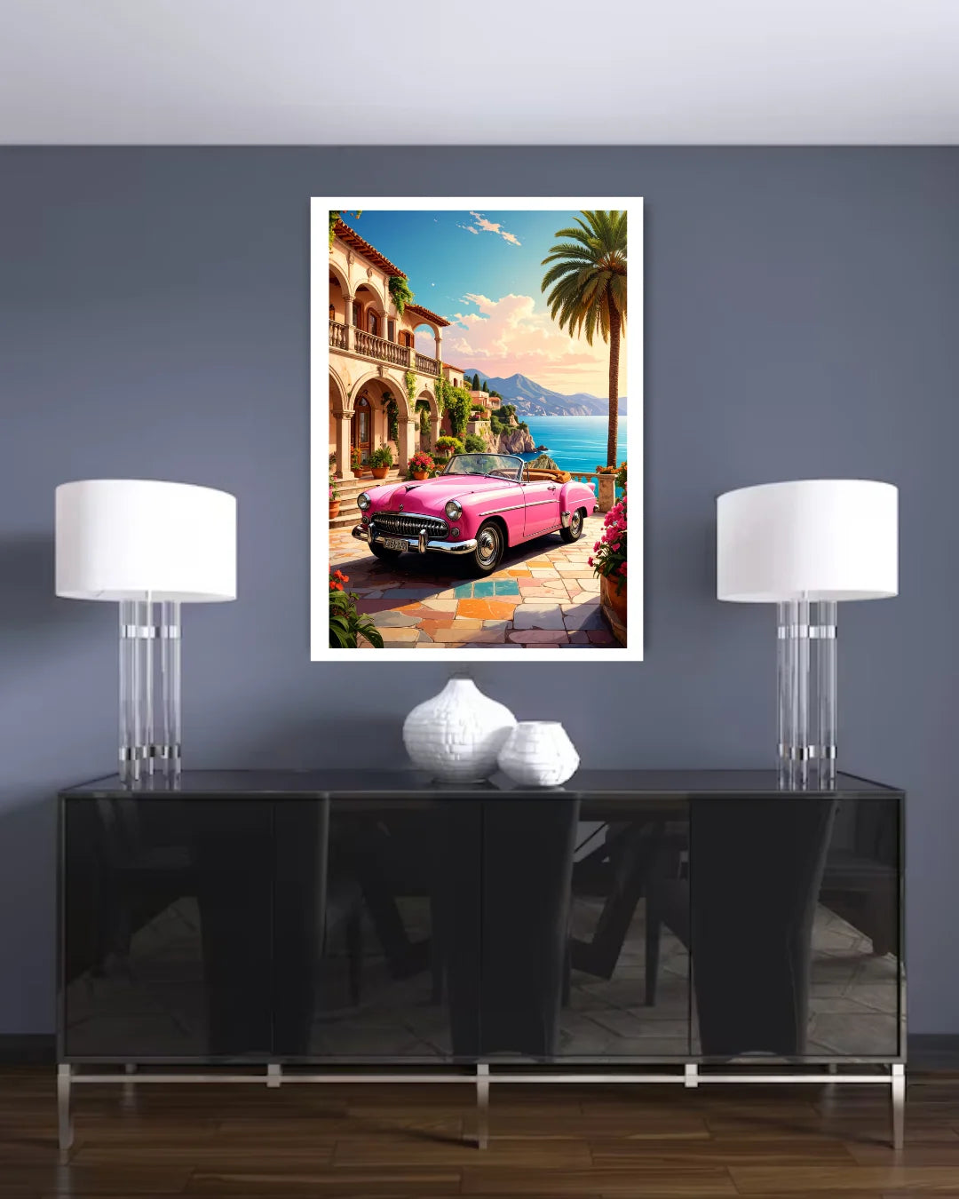 Framed artwork of a pink convertible car on a wall above a black console table with white lamps.