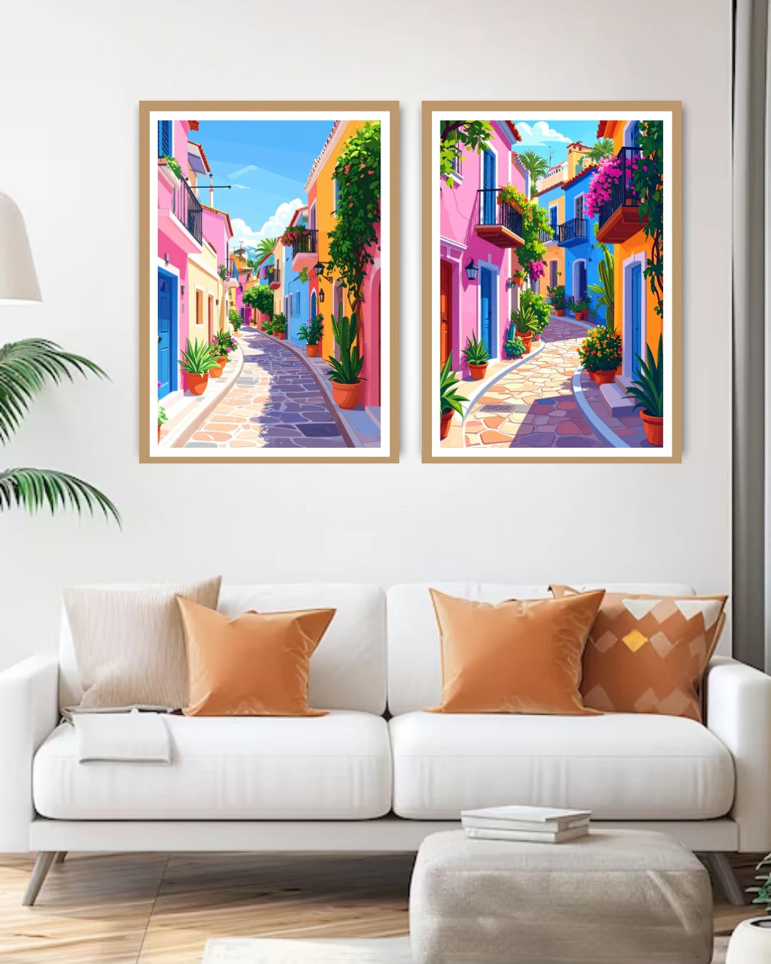 Two colorful framed artworks of a street scene above a white sofa with orange cushions.