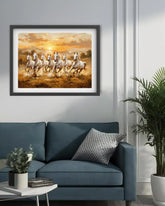 Framed artwork of running horses on a wall above a blue sofa with decorative pillows.