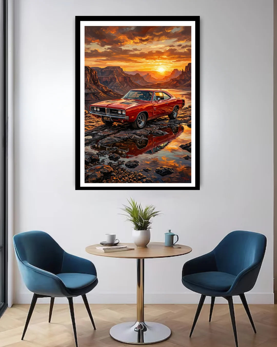 Framed artwork of a red car at sunset over water in a modern room with blue chairs and a small table.