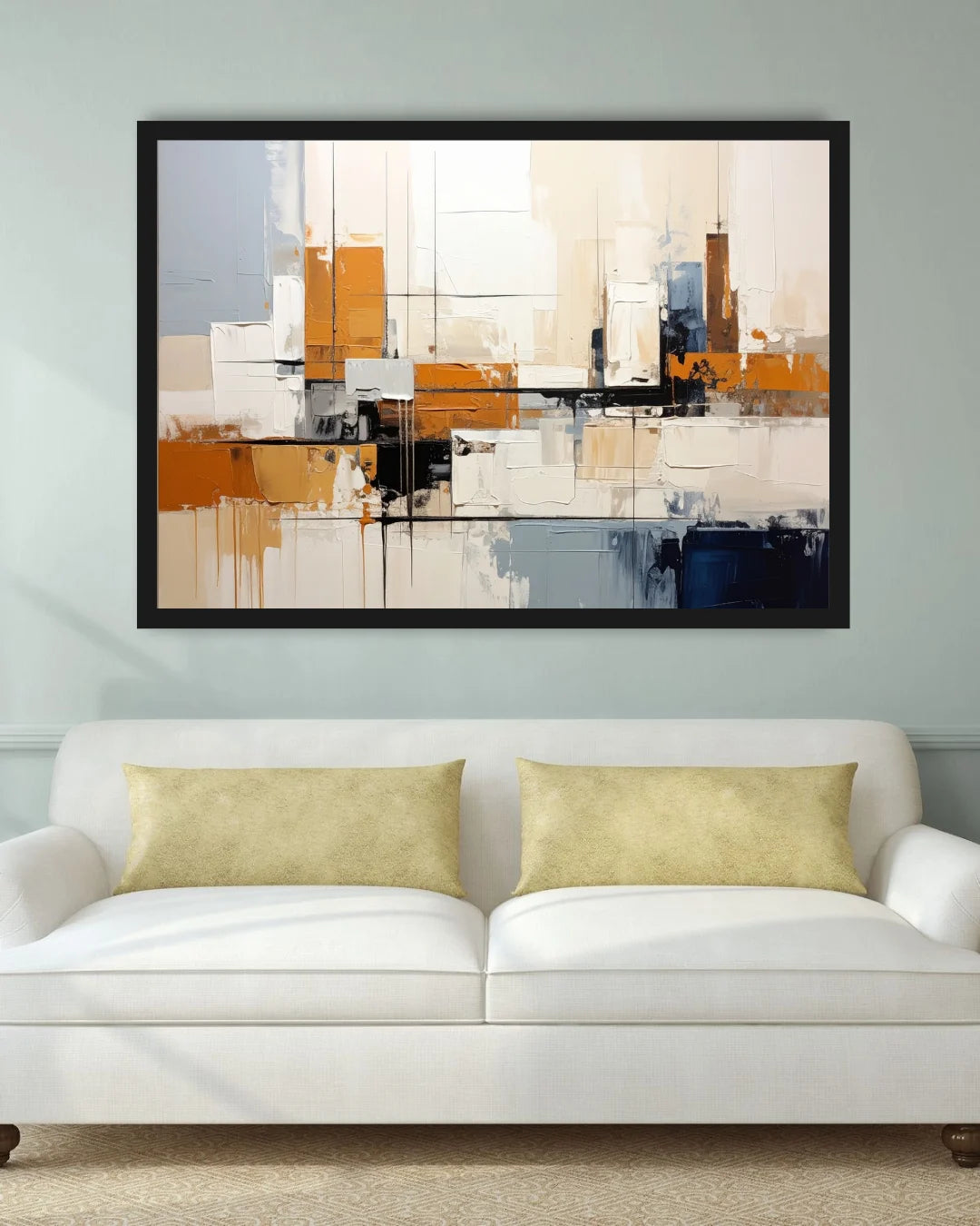 A framed abstract canvas print with geometric blocks of orange, beige, white, black, and blue, displayed on a light gray wall above a white sofa with two gold pillows.