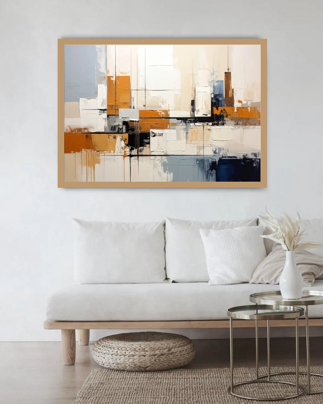 A framed abstract canvas print with geometric shapes in orange, beige, white, gray, and blue, displayed on a white wall above a modern white sofa in a bright living room.