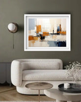 A framed abstract painting with geometric shapes in orange, beige, white, and blue, displayed on a dark olive green wall above a modern textured white sofa in a styled living room.