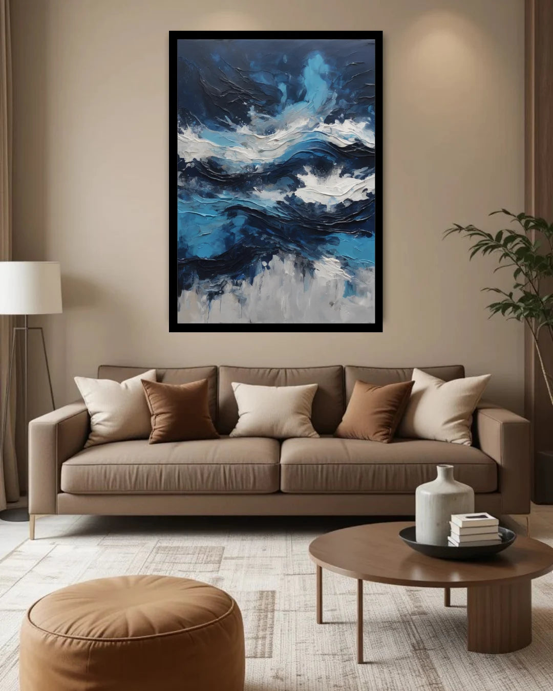 A framed abstract canvas print featuring blue, white, and black waves, displayed on a beige wall above a modern brown sofa in a styled living room.