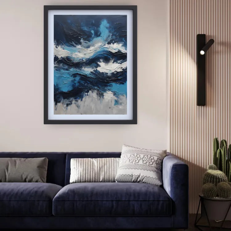 A framed abstract painting of swirling blue, white, and gray waves hangs on a beige wall above a dark blue velvet sofa in a modern living room setting.