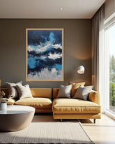 A framed abstract painting with swirling blue, white, and black waves hangs on a dark gray wall above a mustard yellow sectional sofa in a modern living room.
