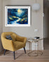 Yellow armchair with a side table and abstract painting of a forest scene on a wall.