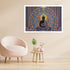A framed wall art print featuring a seated Buddha figure within an ornate mandala design, displayed above a blush pink armchair and a small wooden side table in a styled interior room.