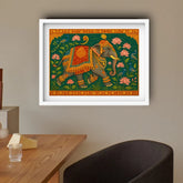 Framed artwork of an elephant with floral decorations on a wall above a wooden table.