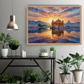 A framed canvas art print depicting a colorful sunset over the Golden Temple in Amritsar, displayed on a light gray wall above a black console table with potted plants.