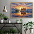 A framed canvas art print depicting a colorful sunset over the Golden Temple in Amritsar, displayed on a light gray wall above a black console table with potted plants.