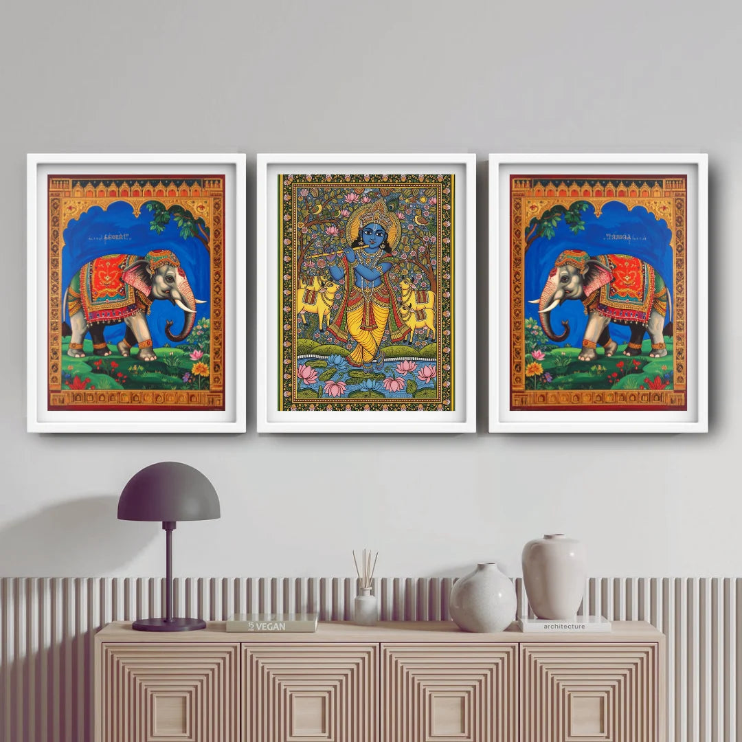 Three colorful framed artworks of elephants and deities on a wall above a cabinet.