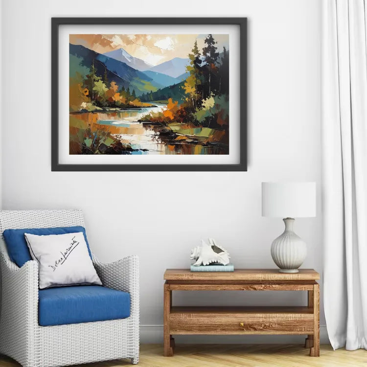 A framed landscape painting of a mountain river scene with autumn foliage, displayed on a white wall above a wicker armchair and a wooden side table with a lamp.