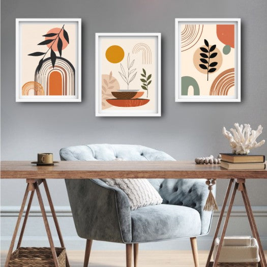 Three framed abstract botanical wall art prints in white frames hang above a wooden desk and a gray velvet armchair in a styled room setting.