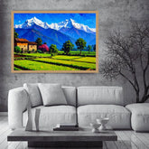 A framed colorful landscape painting of snow-capped mountains, green fields, and a small house, displayed on a gray concrete wall above a white sofa in a modern living room setting.