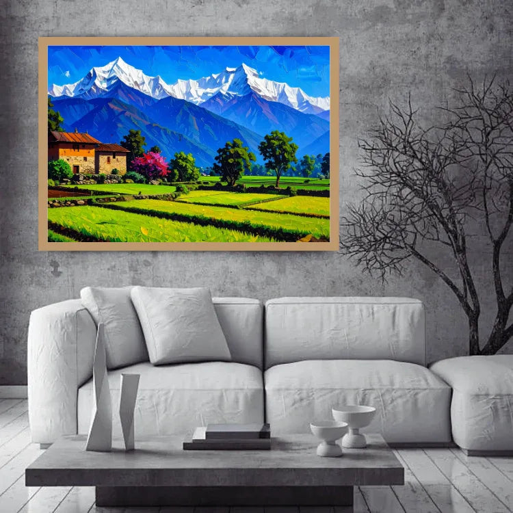 A framed colorful landscape painting of snow-capped mountains, green fields, and a small house, displayed on a gray concrete wall above a white sofa in a modern living room setting.