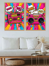 A pair of framed pop-art posters featuring retro boomboxes and comic-style text, displayed above a white sofa in a modern living room setting.