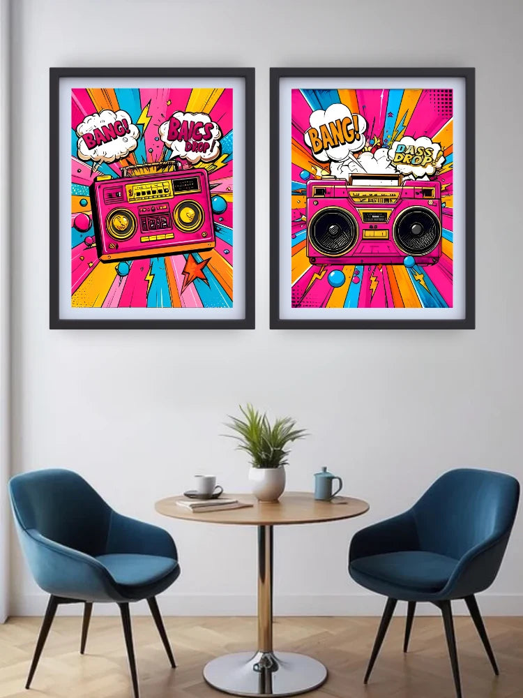 Two framed pop-art posters featuring retro boomboxes and comic-style speech bubbles, displayed on a light gray wall above a small round table with two blue chairs in a modern room setting.