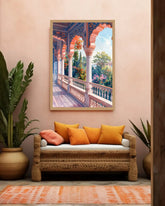 A framed art print depicting a colorful Mediterranean-style arched corridor with lush greenery, displayed on a warm beige wall above a woven rattan sofa with orange and pink pillows.
