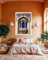 A framed art print depicting an ornate blue and gold architectural niche is displayed on a terracotta-colored wall above a neatly made bed in a modern, warm-toned bedroom.