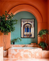 A framed art print depicting an ornate Indian palace balcony with blue and gold details, displayed on a teal wall in a terracotta bathroom setting with a bathtub and potted plants.
