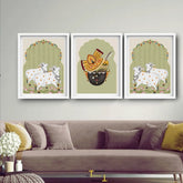 Three framed artworks of cows and a mask on a wall above a sofa.