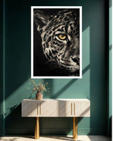 A framed black and white leopard art print with a striking yellow eye hangs on a dark teal wall above a modern white console table with gold legs.