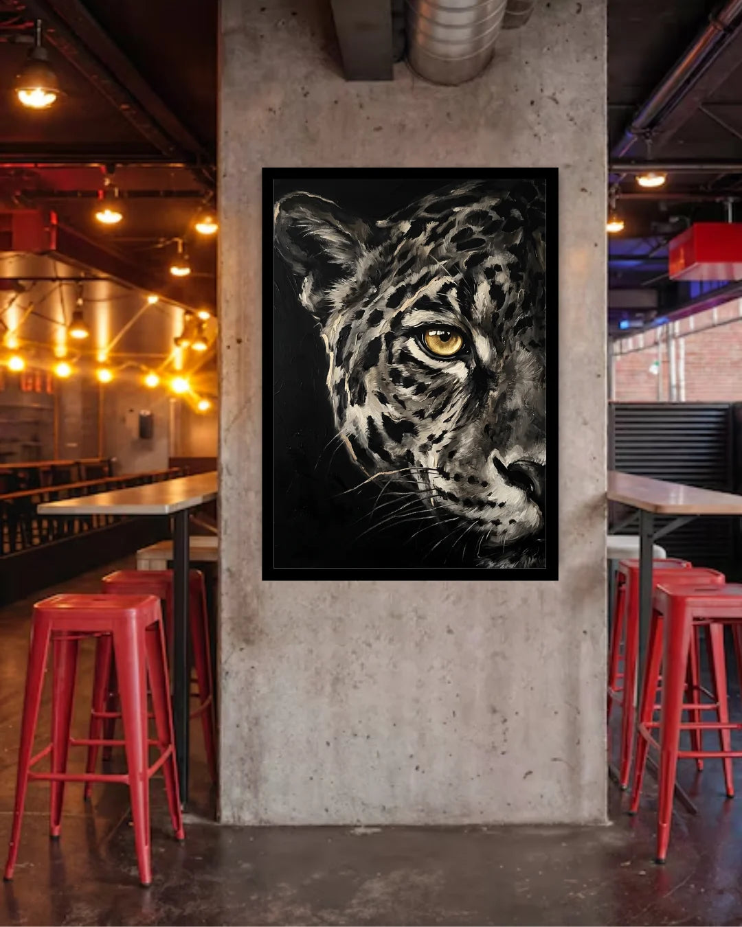 A framed black and white leopard art print hanging on a concrete pillar in a modern industrial bar with red stools and warm hanging lights.