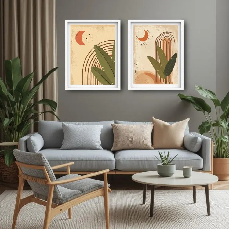 Two framed abstract botanical art prints hang on a gray wall above a light blue sofa in a styled living room with plants, a chair, and a round coffee table.