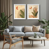 Two framed abstract botanical art prints hang on a gray wall above a light blue sofa in a styled living room with plants, a chair, and a round coffee table.