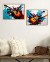 Two framed artworks of guitars with colorful abstract designs on a wall above a wooden shelf.