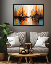 A framed abstract cityscape painting in warm orange, gold, and blue tones hangs on a dark gray wall above two light gray upholstered armchairs with white pillows and a small round wooden coffee table in a styled living room 1