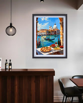 A framed art print depicting a colorful Venetian canal scene with gondolas, domes, and outdoor dining tables, displayed on a light gray wall above a dark wood counter in a modern interior setting.