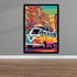 A framed colorful pop-art poster of a vintage Volkswagen camper van driving through a city street, displayed on a gray wall above a wood floor.